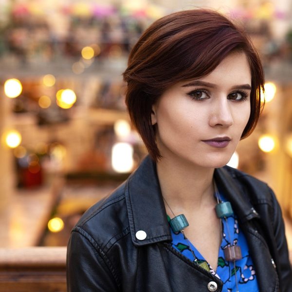 好医生网编辑林砚的工位肖像，短发女性坐在书架前对着笔记本电脑整理选题清单，手边放着写满批注的纸质资料，背景是暖色木质书架与绿植